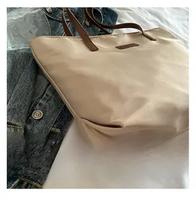 Close-up of the beige nylon tote bag featuring brown leather straps and detailed stitching