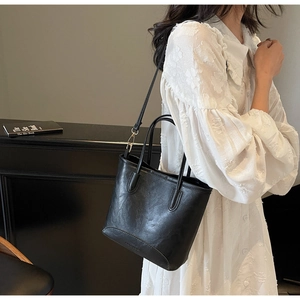 Detail of the black leather bucket bag showing fine texture and detachable strap