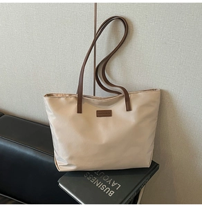 Detail of champagne nylon tote bag showing leather straps and brand logo on a black book