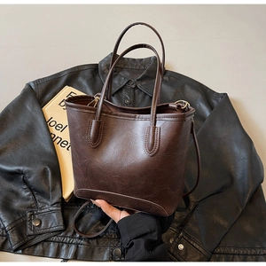Close-up of brown litchi texture tote bag on leather jacket with long shoulder strap