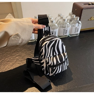 Detail of zebra print crossbody bag with black zippers and adjustable strap held by hand
