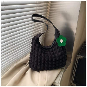 Détail du sac cabas gaufré noir avec breloque fleur verte et textures modernes