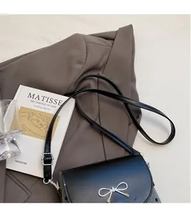 Detail of black crossbody bag with silver bow accent and adjustable smooth shoulder strap