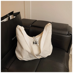 Dettaglio borsa hobo in nylon crema con tracolla larga e targhetta sulla cerniera
