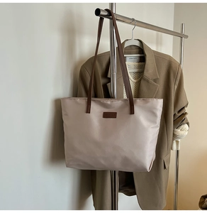 Detail of beige tote bag with brown straps hanging on rack with autumn fashion