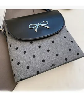 Close-up of black leather flap bag with silver bow detail and grey polka dot wool fabric