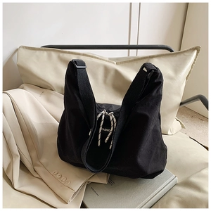 Dettaglio della borsa tote in tela nera con tracolla regolabile ed etichetta moda su fondo morbido