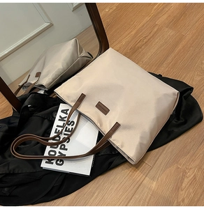 Detail of a large beige tote bag with brown leather straps and fashion label patch