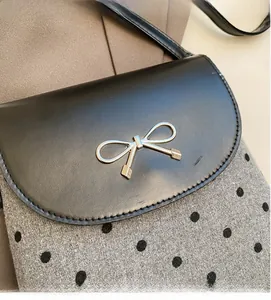 Detailed shot of silver bow buckle on grey polka dot and black leather crossbody bag