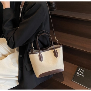 Detail of a two-tone leather tote bag with brown trim and gold hardware on wooden stairs