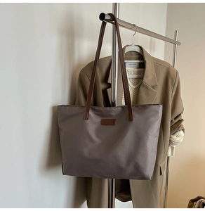 Detail of taupe tote bag with brown straps and logo patch on khaki suit background