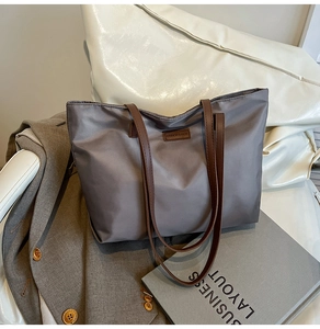 Detail of grey nylon tote bag with leather logo patch and brown shoulder straps