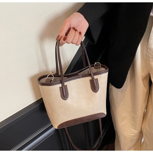 Detail shot of the bottom brand embossing and brown contrast trim on the cream tote bag