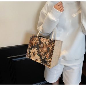 Detail of floral tapestry tote with woven rope handles and linen stitching on a model