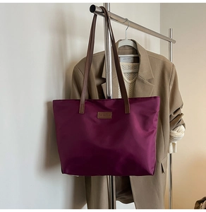 Detail of purple nylon tote bag featuring brown leather handles and a fashion logo patch
