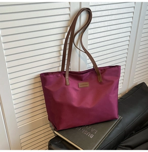 Detail of burgundy tote bag with brown straps placed on a leather sofa by shutters