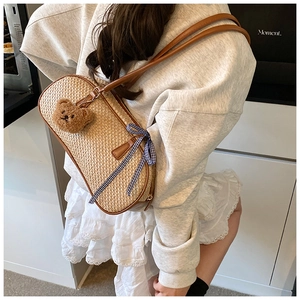 Detail of woven straw handbag with brown leather trim and cute plush bear charm decoration