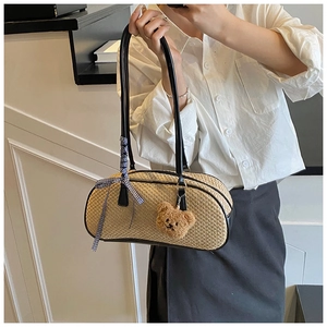 Close-up of beige woven Boston bag featuring black leather trim and a cute teddy bear charm