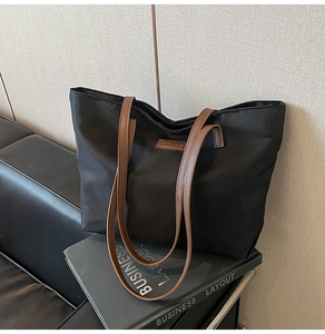 Detail of black nylon tote bag with brown leather straps on a modern leather bench