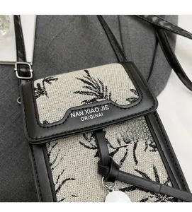 Detail of leaf print canvas and black leather phone bag with a metal charm