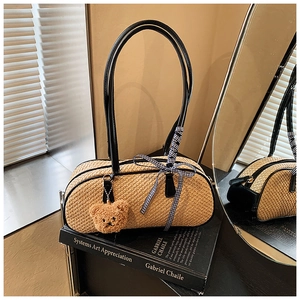 Detail view of woven straw baguette bag with black leather handles and bear pendant