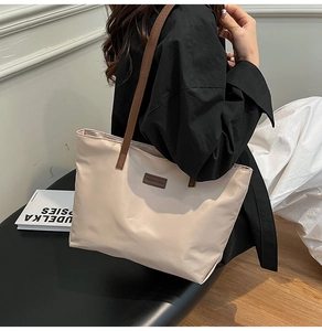 Close-up of a beige large capacity tote bag featuring brown leather straps and fashion label