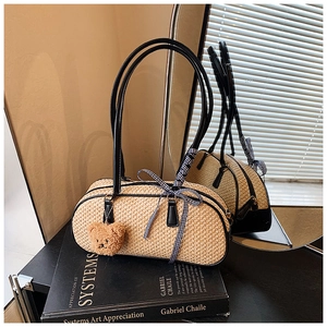 Detail of woven straw tote bag with black leather straps and brown bear charm accessory
