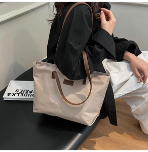 Beige nylon tote bag with brown leather handles worn by a person for daily commuting