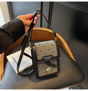 Détail du mini sac de téléphone gris à motif cœurs, bordure en cuir noir et breloque