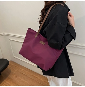Detail of plum purple large tote bag with brown leather handles and fashion logo label