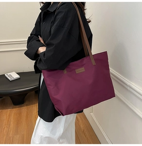 Large burgundy tote bag with brown leather handles shown on model for daily commuting