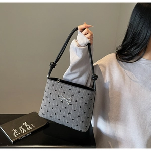 Close-up of grey polka dot handbag featuring a silver bow and knot detail on strap