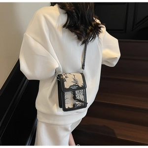 Detail view of canvas crossbody phone bag with black floral patterns on wooden stairs