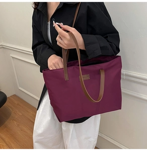 Detailed view of purple nylon tote bag with brown leather handles and brand patch