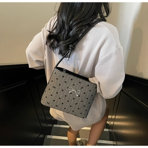 Detail of gray polka dot shoulder bag featuring a decorative silver bow and knotted strap