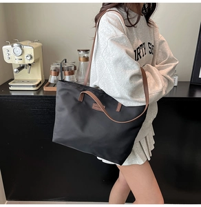 Close-up of black nylon tote bag with brown leather straps shown in a modern cafe setting