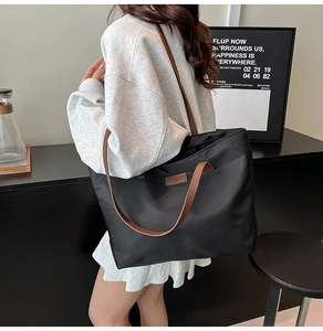 Large black nylon tote bag with brown leather straps shown on shoulder in a modern setting