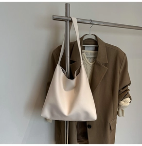Detail of a large cream tote bag with smooth leather texture hanging with brown blazer
