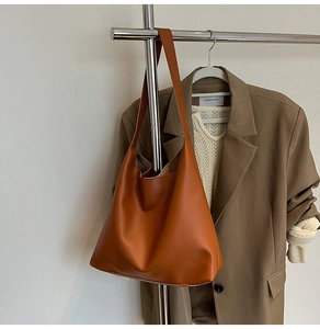 Brown faux leather tote bag hanging on metal rack with earthy autumn outfit background