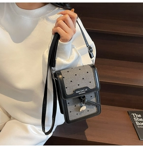 Détail de la mini pochette grise à motif cœurs, bordure en cuir et breloque en métal