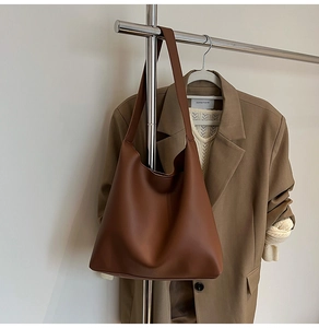 Minimalist brown leather tote bag with wide strap hanging on clothes rack