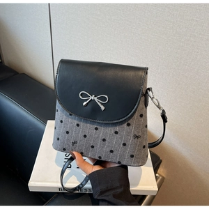Détail du sac seau en tricot gris avec rabat en cuir noir et accessoire nœud argenté