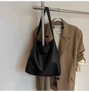 Detail of a black large-capacity leather Hobo bag hanging against a brown blazer background