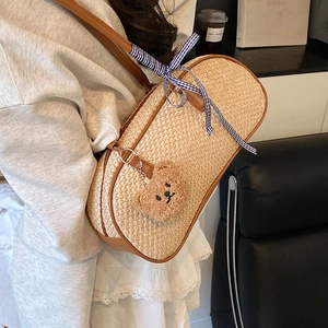 Woven straw shoulder bag with brown leather trim and cute teddy bear charm on model