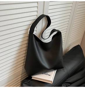 Minimalist black leather tote bag displayed on a sleek base with an aesthetic book setup