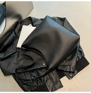 Flat-lay detail of a large minimalist black matte leather tote bag on casual apparel