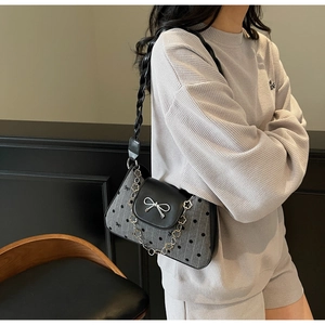 Detail of grey polka dot texture handbag featuring silver bow and floral chain strap