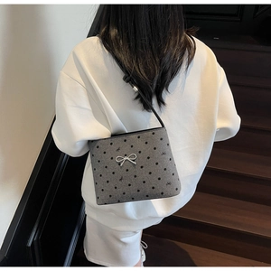 Detail view of grey polka dot felt bag with metallic bow and black leather strap