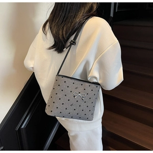 Detailed view of grey polka dot bucket bag with silver metal bow and black leather strap