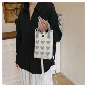 Detail of knitted heart pattern phone bag with round black button closure and handles
